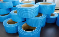 新製品の粘着剤付き薄葉紗細幅テープは、薄い寒冷紗と薄いフィルムを貼り合わせている。建築資材や壁ひび割れ補強材として使われる